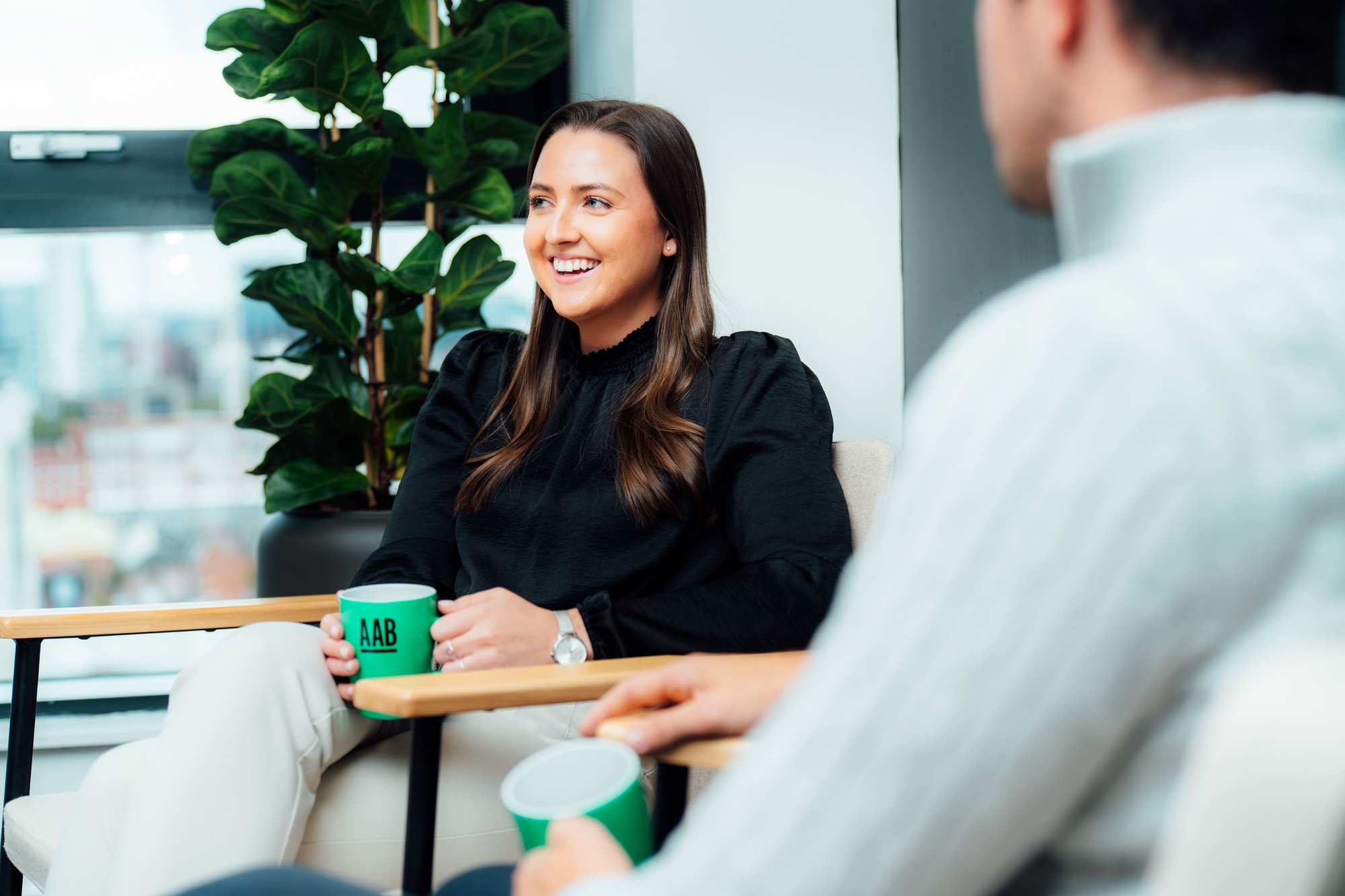 An image of Lori Young sitting on an office chair and holding an AAB mug.