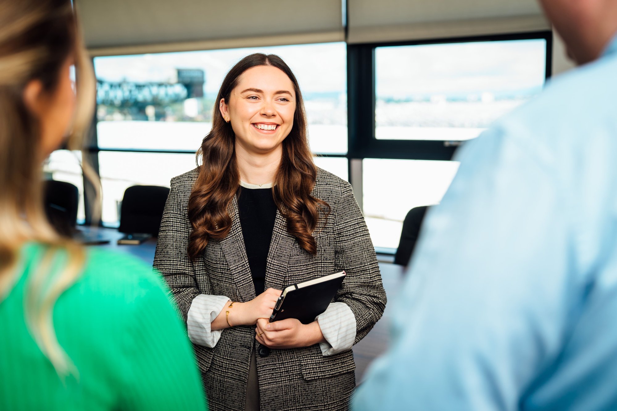 An image of Zoe Dollard smiling at her colleagues wearing a blazer and smiling at the camera. 